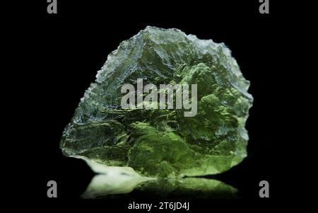 Pierre moldavite isolée sur fond noir. Gros plan d'une pierre précieuse tchèque verte. Véritable verre de tektite naturel. Banque D'Images