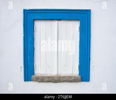 Fenêtre traditionnelle de l'Algarve dans une maison typique à Portimão. Fenêtre en bois peinte en blanc avec garniture bleue et mur blanc. Banque D'Images