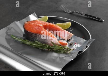 Feuille d'aluminium avec poisson cru, citron vert, romarin et épices sur table grise. Cuisson du saumon Banque D'Images