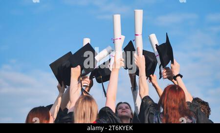 Les diplômés collégiaux élèvent leurs casquettes et leurs diplômes à la hausse. Banque D'Images