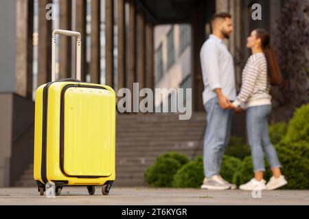 Relation longue distance. Jeune couple tenant la main près du bâtiment à l'extérieur, concentrez-vous sur la valise jaune Banque D'Images