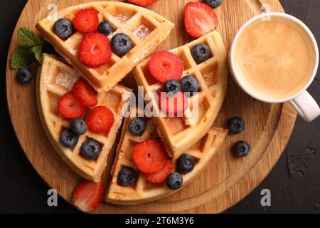 Gaufres belges savoureuses avec des baies fraîches et une tasse de café sur la table noire, vue de dessus Banque D'Images