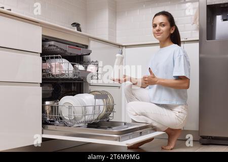 femme verse le liquide de rinçage dans le compartiment lave-vaisselle dans la cuisine blanche moderne Banque D'Images