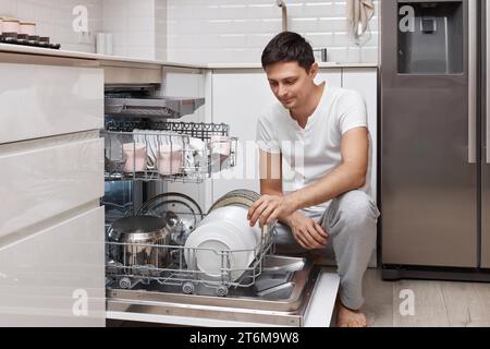 bel homme positif mettant des assiettes dans la machine à lave-vaisselle dans la cuisine Banque D'Images