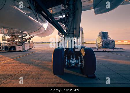 Train d'atterrissage de grand avion. Préparation avion cargo avant le vol au beau coucher du soleil. Déchargement et chargement de conteneurs de fret à l'aéroport. Banque D'Images