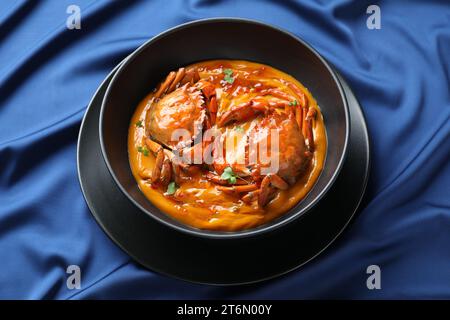 Délicieux crabes bouillis avec sauce dans un bol sur une nappe bleue Banque D'Images