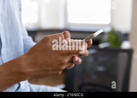 Gros plan des mains masculines tapant sur le téléphone portable à l'intérieur Banque D'Images