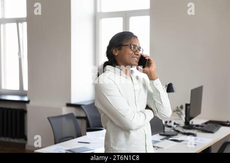 Heureux homme d'affaires indien parlant sur le téléphone portable dans le bureau Banque D'Images