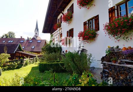 Scène idyllique avec une ferme traditionnelle bavaroise rustique alpine avec des géraniums rouges et un tas de bois de chauffage par le mur à Schwangau dans les Alpes bavaroises Banque D'Images
