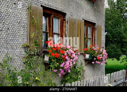 Maison de campagne traditionnelle bavaroise alpine couverte de bardeaux de bois avec géraniums sur le rebord de la fenêtre dans les Alpes bavaroises le jour de septembre à Unterjoch Banque D'Images