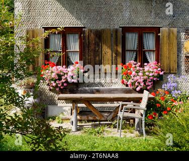 Maison de campagne traditionnelle bavaroise alpine couverte de bardeaux de bois avec géraniums sur le rebord de la fenêtre dans les Alpes bavaroises le jour de septembre à Unterjoch Banque D'Images