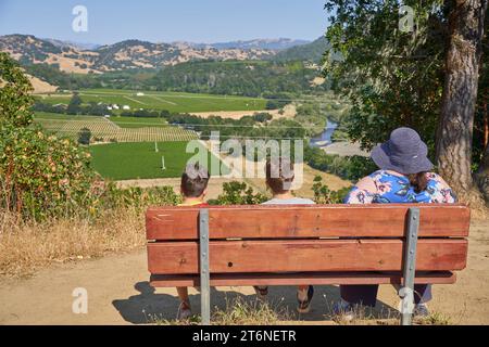 Mère et ses deux garçons assis sur un banc, profitant d'une vue élevée sur une vallée avec des vignes près de la rivière russe, à Healdsburg, en Californie. Banque D'Images