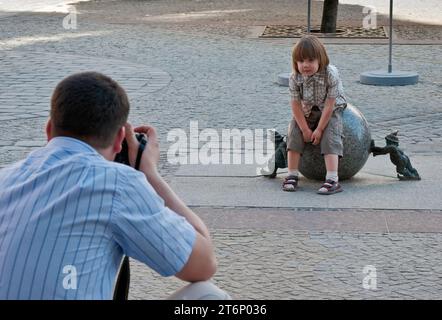 Papa prenant des photos d'enfant à la sculpture de ball-poussant et soulevant des nains Sisyphe près de Rynek (place du marché) à Wrocław, Basse-Silésie, Pologne Banque D'Images