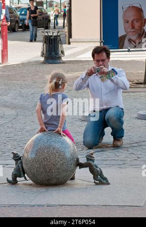 Papa prenant des photos d'enfant à la sculpture de ball-poussant et soulevant des nains Sisyphe près de Rynek (place du marché) à Wrocław, Basse-Silésie, Pologne Banque D'Images