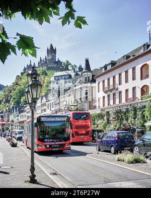 Bus et circulation automobile sur la rue principale de Cochem Allemagne avec le château de Reichsburg au-dessus de la ville touristique médiévale. Un must à voir sur la Moselle. Banque D'Images