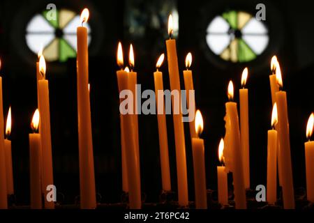 Plusieurs bougies allumées se tiennent au centre de deux vitraux, l'un avec un rayon de soleil qui brille à travers Banque D'Images