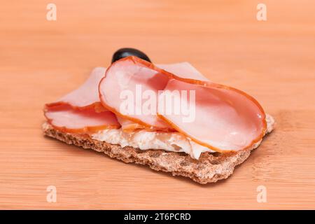 Pain de croustillant aux grains entiers avec jambon, fromage à la crème et olives sur planche à découper en bambou. Petit déjeuner facile. Alimentation. Sandwichs rapides et sains. Croustillant et garniture savoureuse. En-cas diététiques Banque D'Images