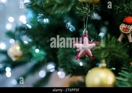 Étoile rose accrochée sur une branche verte d'un arbre de Noël parmi les boules et les guirlandes Banque D'Images