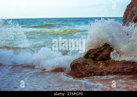 La vague de la mer bat contre une pierre sur le rivage. Mer bleue et rivage rocheux. Banque D'Images