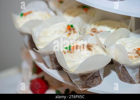 Gâteaux de tasse de chocolat avec tourbillon de rasberry et fruits de rasberry sur le dessus cupcakes avec glaçage à la vanille et garnitures de carottes sur la table de dessert Banque D'Images