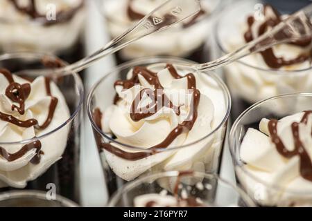 Rangées de chocolat et fouetter desserts à la crème avec des tourbillons dans de petites tasses en plastique avec garnitures de biscuits au chocolat à la table de dessert dans de petites tasses en plastique wi Banque D'Images