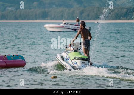 Homme très bien en forme conduire en toute sécurité jet ski du rivage à la mer ouverte. Station balnéaire tropicale. PHUKET, THAÏLANDE - 30 AVRIL 2023 Banque D'Images