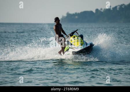 Homme très bien en forme conduire en toute sécurité jet ski de la mer à la rive. Station balnéaire tropicale. PHUKET, THAÏLANDE - 30 AVRIL 2023 Banque D'Images