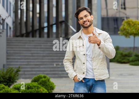 J'aime. Homme indien heureux soulève les pouces vers le haut est d'accord avec quelque chose donne une réponse positive recommande la publicité aime bonne idée rétroaction célébrant la victoire de succès. Gars arabe dans la rue de la ville. Copy-space Banque D'Images