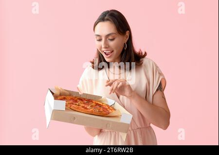 Jeune femme tenant une boîte en carton avec une pizza savoureuse sur fond rose Banque D'Images