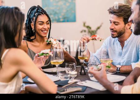 Un groupe d'amis partageant des rires et de la bonne nourriture autour d'une table, avec des verres à vin levés, profitant de la compagnie de l'autre - repas de groupe avec pizza et Banque D'Images
