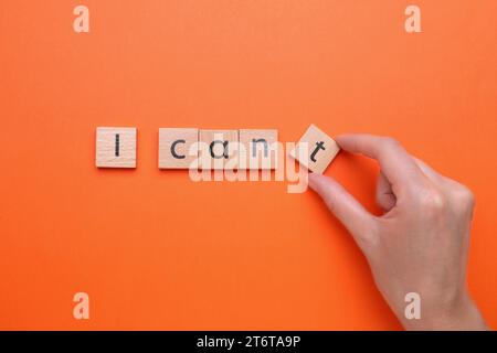 Concept de motivation. Femme changeant la phrase de Je ne peux pas en Je peux en enlevant le carré en bois avec la lettre T sur fond orange, vue de dessus Banque D'Images