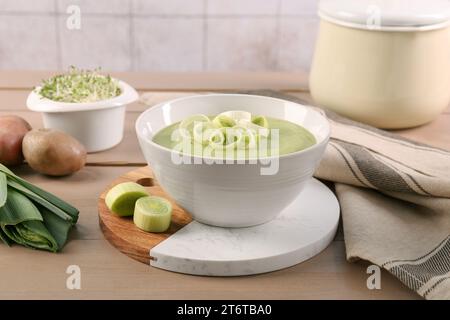 Soupe savoureuse de poireaux dans un bol et ingrédients frais sur une table en bois Banque D'Images