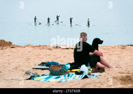 Un homme et son chien sur la plage regardent un groupe de paddleboarders passer dans la baie de Barafundle dans le sud du pays de Galles Banque D'Images