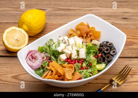 Un bol en céramique blanche rempli d'une salade colorée avec une fourchette et deux citrons en arrière-plan est représenté Banque D'Images