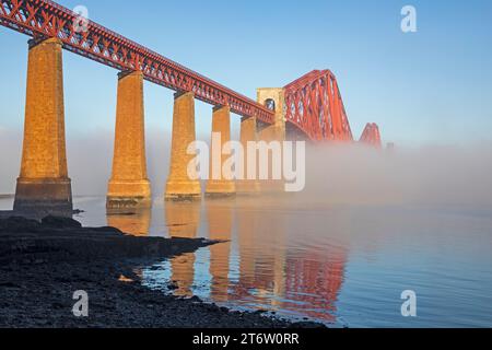 South Queensferry, Édimbourg, Écosse, Royaume-Uni. 12 novembre 2023. Le Forth Rail Bridge rouge coquelicot élimine progressivement la couverture de brouillard glacial alors que le soleil matinal le brûle et reflète la structure emblématique du Firth of Forth. La température a commencé à moins 4 degrés centigrades augmentant à 6 degrés à 10 heures du matin. Crédit : Archwhite/alamy Live News. Banque D'Images