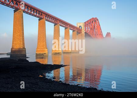 South Queensferry, Édimbourg, Écosse, Royaume-Uni. 12 novembre 2023. Le Forth Rail Bridge rouge coquelicot élimine progressivement la couverture de brouillard glacial alors que le soleil matinal le brûle et reflète la structure emblématique du Firth of Forth. La température a commencé à moins 4 degrés centigrades augmentant à 6 degrés à 10 heures du matin. Crédit : Archwhite/alamy Live News. Banque D'Images