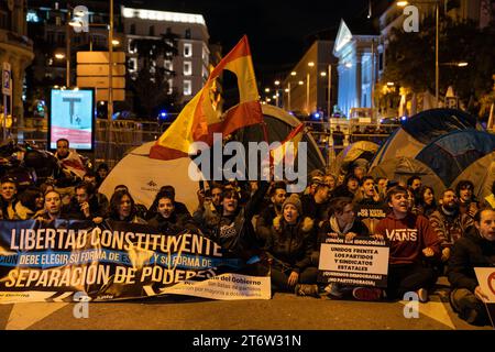 Les manifestants brandissent des drapeaux espagnols, des pancartes de banderoles exprimant leur opinion près d'un groupe de tentes pendant la manifestation. Concentration et tentative de camping ont eu lieu devant le Congrès des députés à Madrid sous le slogan ¨mettons des limites et un contrôle sur les politiciens¨, organisé par ¨la Junta Democrática¨, une organisation civile qui coordonne et promeut l'action unitaire du peuple espagnol. L'objectif est d'établir librement et pacifiquement en Espagne un régime démocratique avec une séparation des pouvoirs dès le départ et l'élection directe des représentants politiques. Banque D'Images