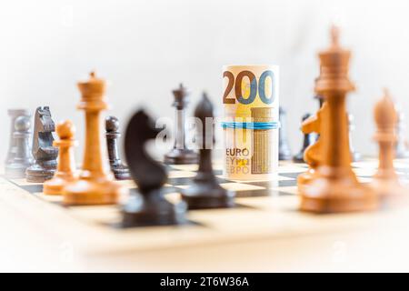 Jeu d'échecs avec des pièces d'échecs floues à bord avec des billets roulés de 200 euros avec du caoutchouc bleu bann. Photo de haute qualité Banque D'Images