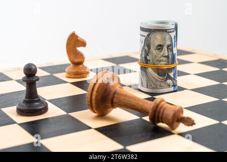 Jeu d'échecs et billets d'un dollar roulé comme une pièce d'échecs, roi blanc vaincu. . Photo de haute qualité Banque D'Images