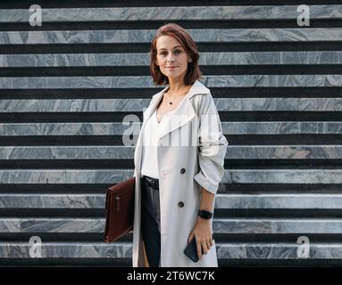 Élégante femme d'âge moyen entrepreneur tenant un dossier en cuir debout à l'extérieur Banque D'Images