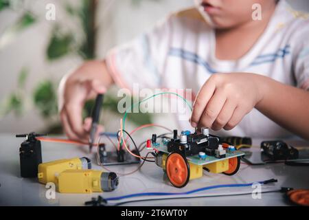 Un enfant asiatique branche le câble d'énergie et de signal à la puce de capteur avec la voiture robot Arduino Banque D'Images