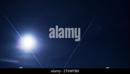 Des sentiers de condensation, majestueux et fugaces, flottent doucement sous un soleil flamboyant dans un ciel bleu profond. Banque D'Images