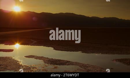 Au coucher du soleil, le soleil d'été s'abat sur les eaux de surface stagnantes du bassin Badwater dans le parc national de la Vallée de la mort. Banque D'Images