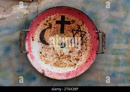 Un vieux wok en métal est monté sur un mur et peint avec les symboles de l'Islam, du Christianisme et du Judaïsme comme signe de coexistence religieuse à Acre, ISR Banque D'Images