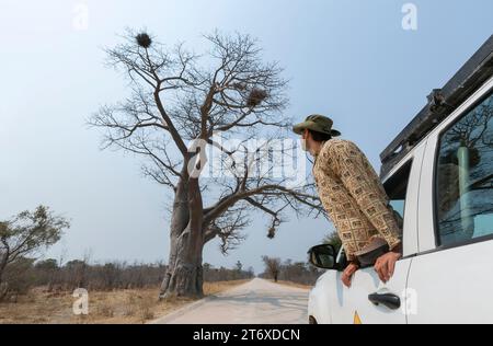 Jeune touriste regardant le paysage africain par la fenêtre de sa voiture blanche tout-terrain garée. Banque D'Images