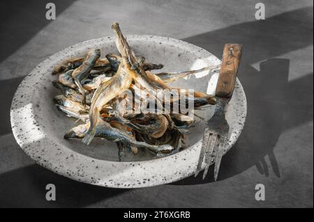 Éperlan salé séché. Baltic séché sentait sur une assiette d'argile ronde faite à la main, un apéritif pour la bière. Lumière dure. Banque D'Images