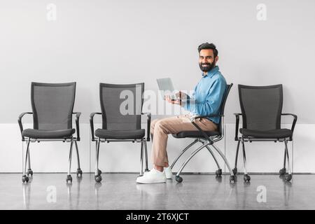 Homme indien joyeux avec ordinateur portable dans la salle d'attente Banque D'Images