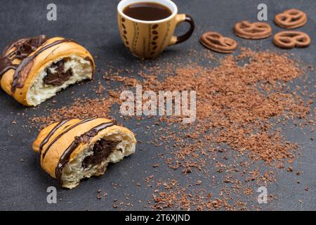 Deux moitiés de croissant au chocolat, tasse de café, saupoudrages de chocolat. Fond noir. Vue de dessus. Espace de copie Banque D'Images