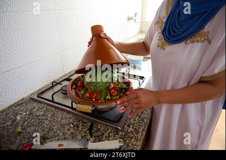 Gros plan femme au foyer du Moyen-Orient avec la tête couverte de hijab, debout par le poêle, cuisinant tajine marocain avec des légumes frais biologiques dans la cuisine à Banque D'Images