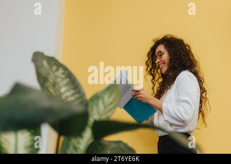 Une employée adorable, aux cheveux bouclés, analyse les rapports, fait de la paperasse et s'engage dans la résolution créative de problèmes pour stimuler la rentabilité et la croissance. Banque D'Images